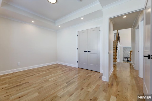 unfurnished bedroom featuring ornamental molding, a closet, a raised ceiling, and light wood-type flooring