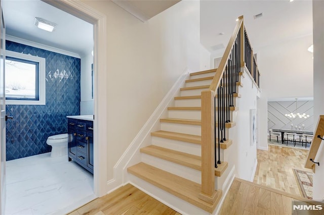 stairs featuring a chandelier, crown molding, and wood-type flooring