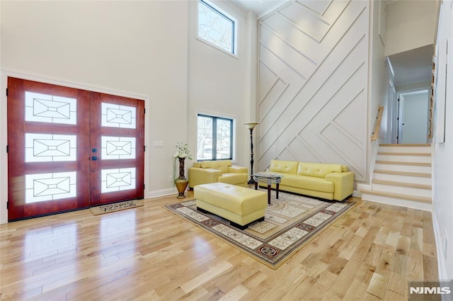 foyer with french doors, a towering ceiling, and light wood-type flooring