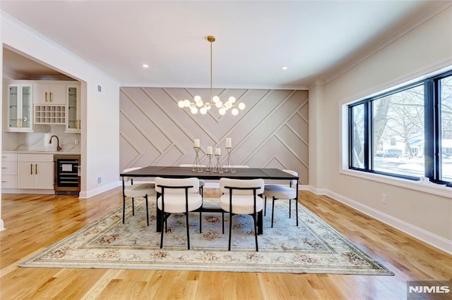 dining room with beverage cooler, light hardwood / wood-style flooring, crown molding, and a notable chandelier