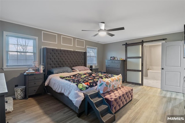 bedroom featuring hardwood / wood-style floors, ensuite bath, ceiling fan, and a barn door