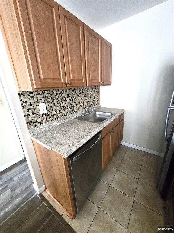 kitchen with sink, dishwasher, dark tile patterned flooring, and decorative backsplash