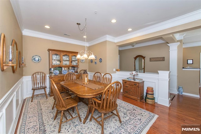 dining room featuring ornate columns, light wood-type flooring, ornamental molding, and an inviting chandelier