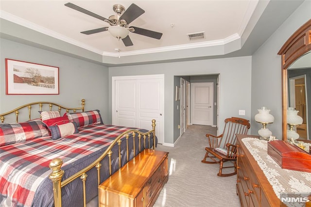 carpeted bedroom with a closet, ceiling fan, crown molding, and a tray ceiling