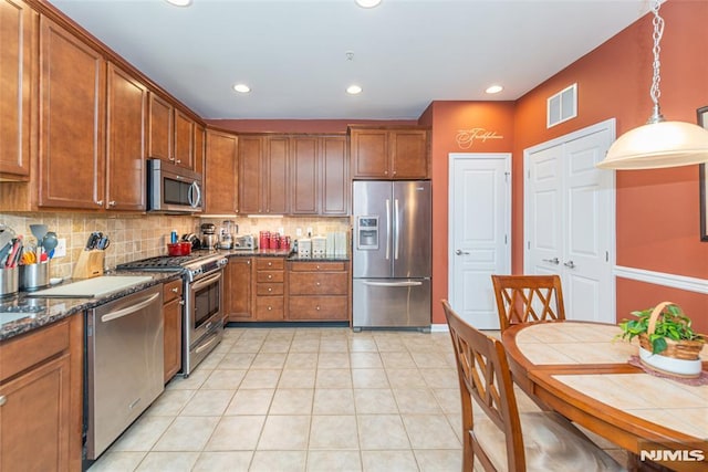 kitchen with appliances with stainless steel finishes, decorative light fixtures, backsplash, dark stone counters, and light tile patterned flooring