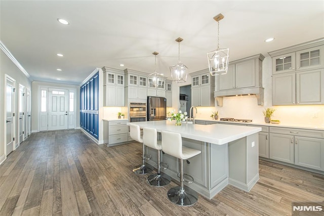 kitchen with gray cabinets, appliances with stainless steel finishes, a kitchen bar, a kitchen island with sink, and dark wood-type flooring