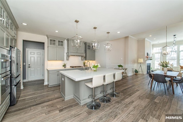 kitchen with pendant lighting, gray cabinetry, a chandelier, dark hardwood / wood-style flooring, and a kitchen island with sink