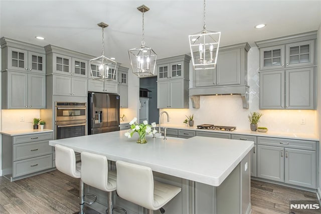 kitchen featuring gray cabinets, appliances with stainless steel finishes, dark hardwood / wood-style floors, pendant lighting, and an island with sink