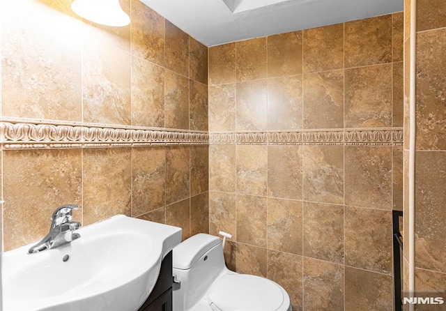 bathroom featuring toilet, vanity, and tile walls