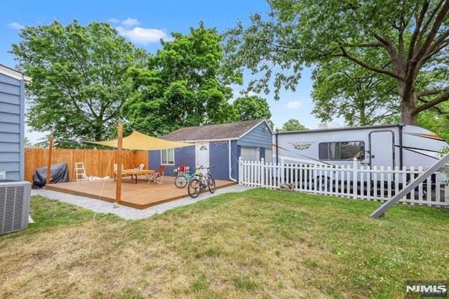 back of property featuring a deck, a lawn, central AC, and a storage shed