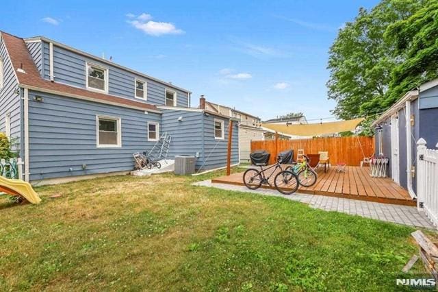 rear view of property featuring central AC unit, a wooden deck, and a yard