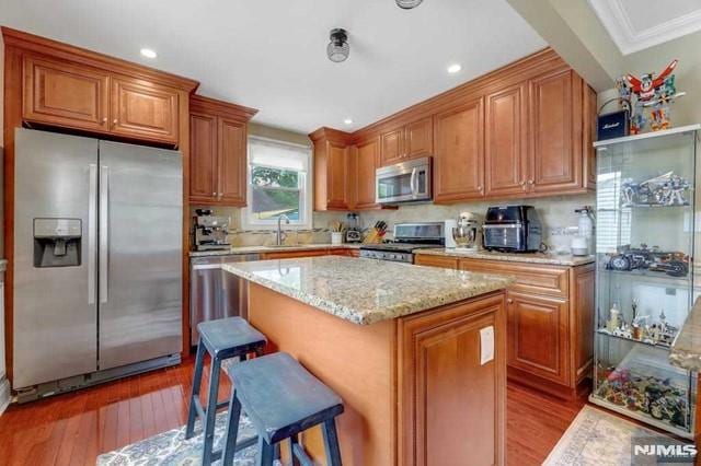 kitchen with appliances with stainless steel finishes, a center island, wood-type flooring, a kitchen breakfast bar, and crown molding