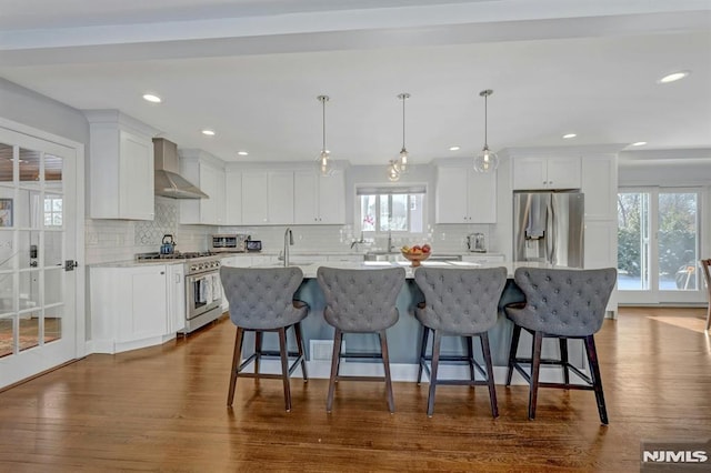 kitchen with white cabinetry, appliances with stainless steel finishes, wall chimney exhaust hood, and a kitchen island with sink