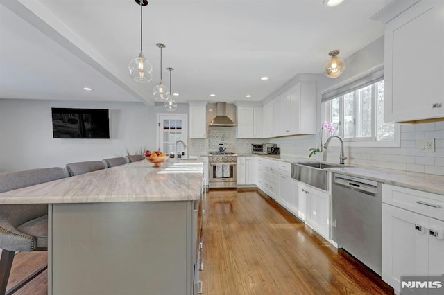 kitchen with white cabinetry, stainless steel appliances, wall chimney exhaust hood, and an island with sink