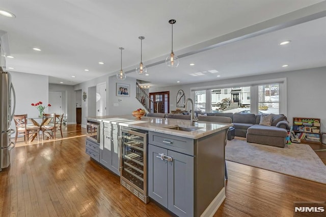 kitchen with gray cabinets, a center island with sink, pendant lighting, and wine cooler