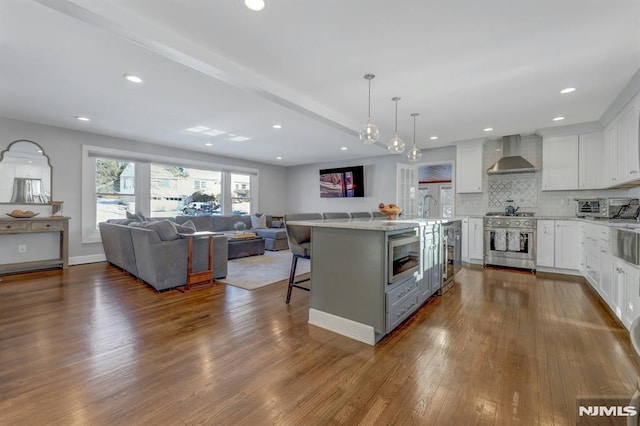 kitchen featuring white cabinetry, wall chimney range hood, stainless steel appliances, a kitchen breakfast bar, and hanging light fixtures