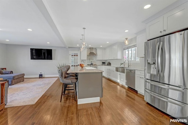 kitchen featuring a center island, appliances with stainless steel finishes, white cabinetry, decorative backsplash, and wall chimney exhaust hood