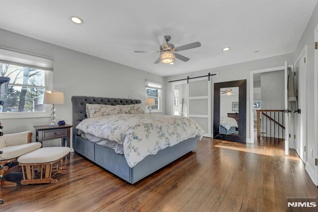 bedroom with dark wood-type flooring, ceiling fan, and a barn door