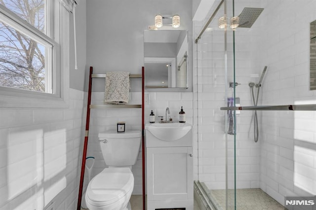 bathroom with an enclosed shower, toilet, vanity, and tile walls