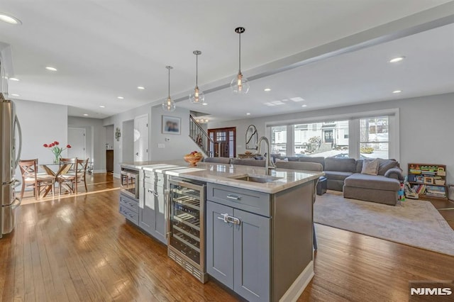 kitchen featuring hanging light fixtures, a kitchen island with sink, gray cabinetry, and beverage cooler