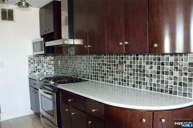 kitchen with tasteful backsplash, gas stove, light tile patterned flooring, and wall chimney exhaust hood