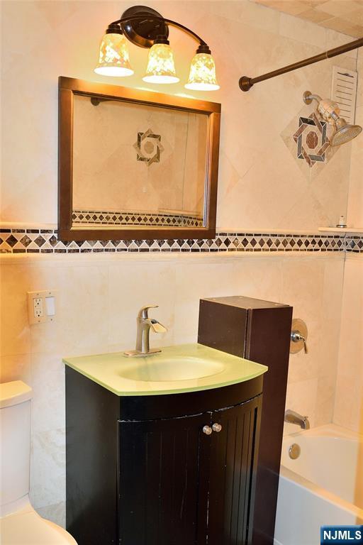 full bathroom featuring vanity, tile walls, toilet, and washtub / shower combination