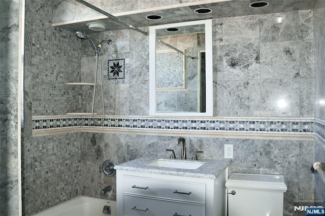 full bathroom featuring vanity, tiled shower / bath combo, tile walls, and toilet