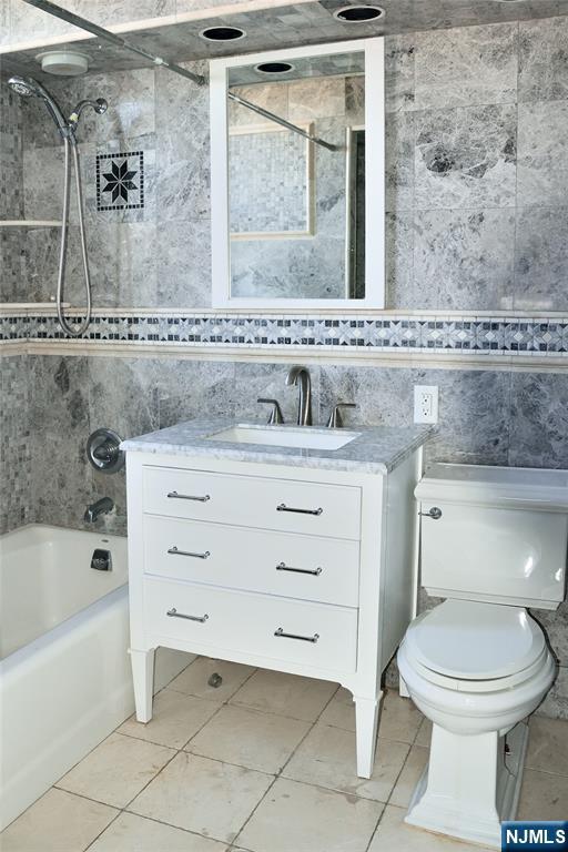 full bathroom with tile walls, vanity, tiled shower / bath, and toilet