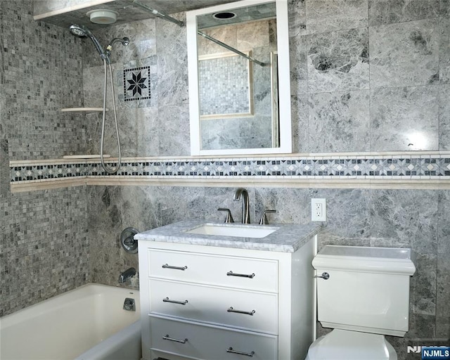 full bathroom featuring tile walls, vanity, tiled shower / bath, and toilet