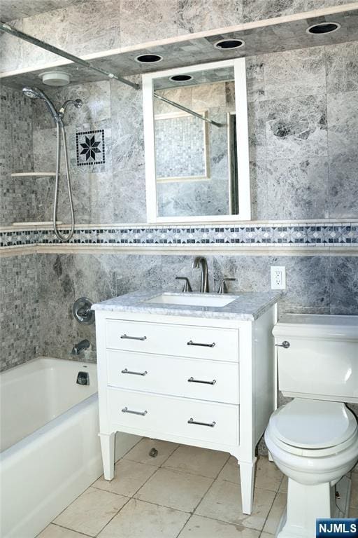 full bathroom featuring tiled shower / bath, vanity, toilet, and tile walls