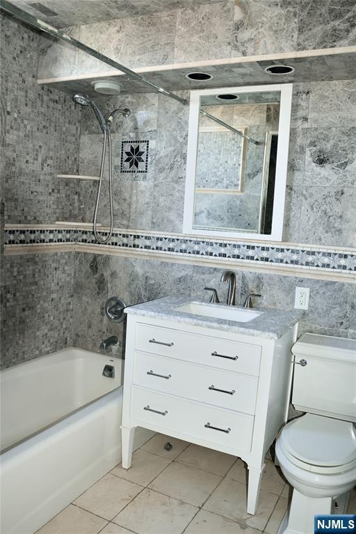 full bathroom featuring tiled shower / bath combo, vanity, tile walls, and toilet