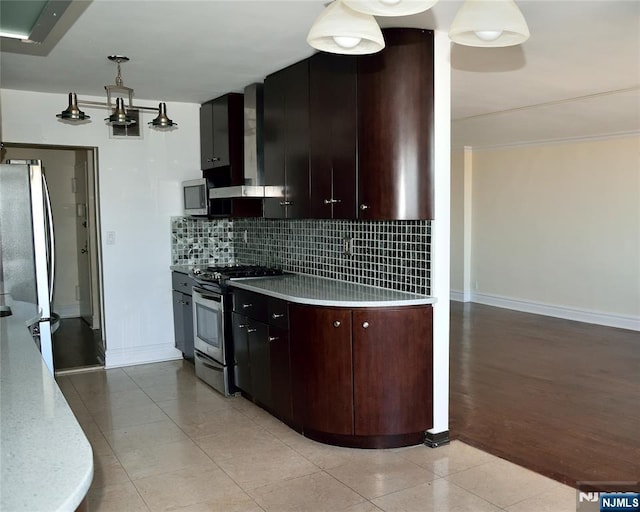 kitchen featuring pendant lighting, appliances with stainless steel finishes, backsplash, light tile patterned flooring, and wall chimney exhaust hood