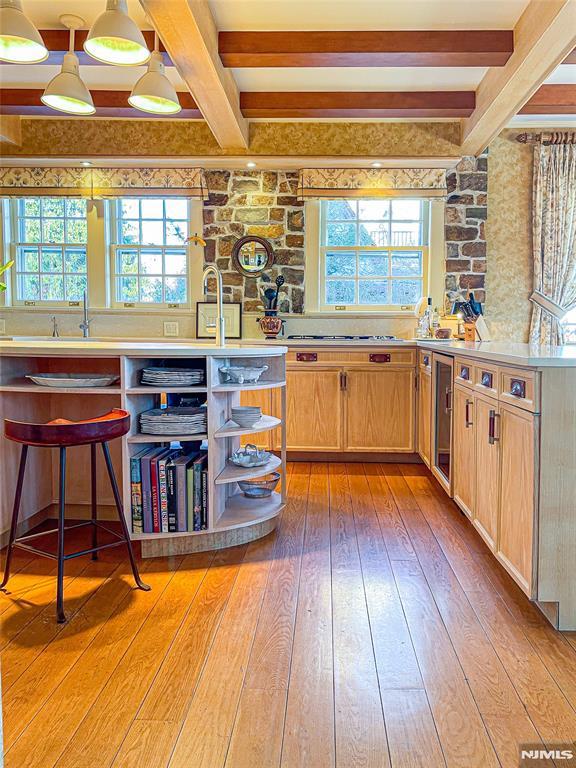 kitchen featuring decorative light fixtures, hardwood / wood-style floors, light brown cabinets, and beam ceiling