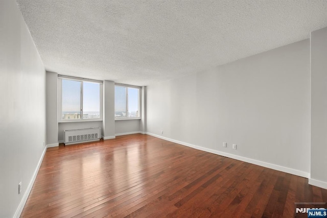 unfurnished room featuring hardwood / wood-style flooring, radiator, and a textured ceiling