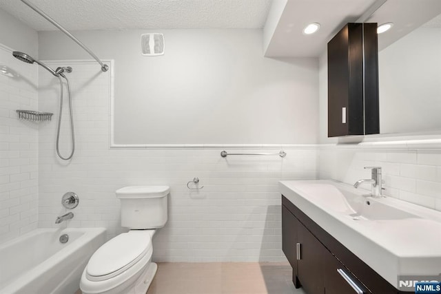 full bathroom featuring tile walls, tiled shower / bath combo, vanity, toilet, and a textured ceiling