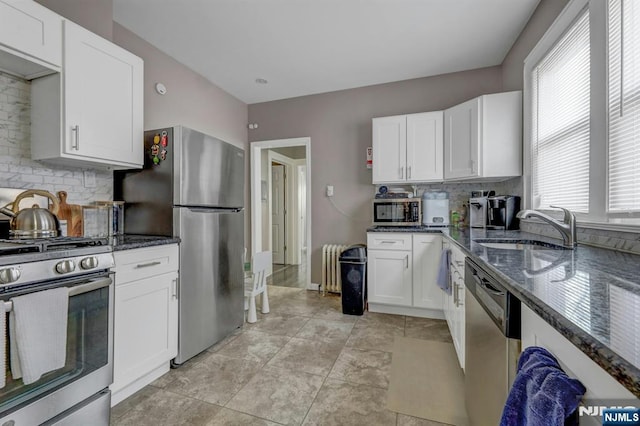 kitchen with sink, appliances with stainless steel finishes, white cabinetry, backsplash, and dark stone counters