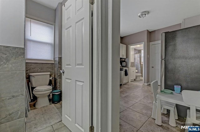 bathroom with toilet, tile patterned flooring, and tile walls