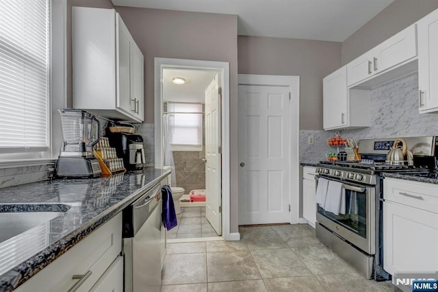 kitchen featuring stainless steel appliances, light tile patterned floors, white cabinets, and dark stone counters