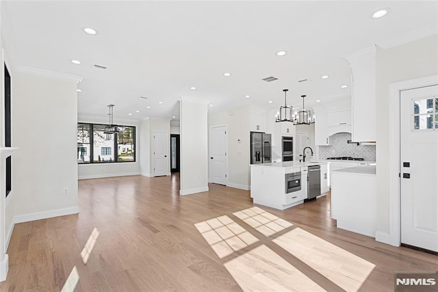 kitchen with white cabinets, stainless steel appliances, hanging light fixtures, and a kitchen island with sink