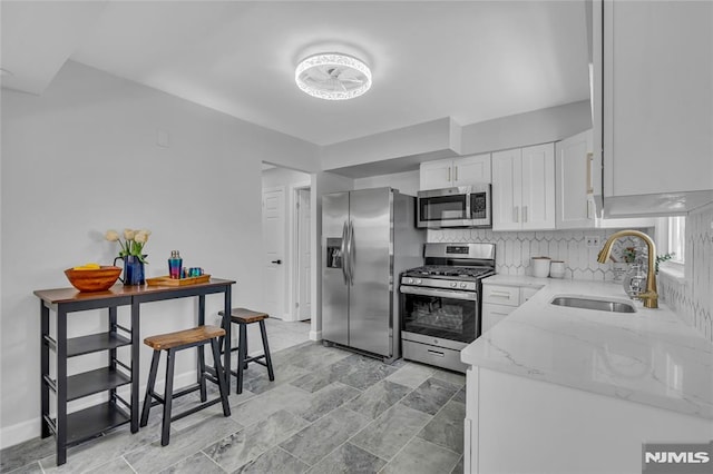 kitchen with light stone countertops, white cabinets, stainless steel appliances, sink, and backsplash