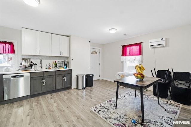 kitchen featuring stainless steel dishwasher, sink, white cabinetry, light hardwood / wood-style floors, and a wall mounted AC