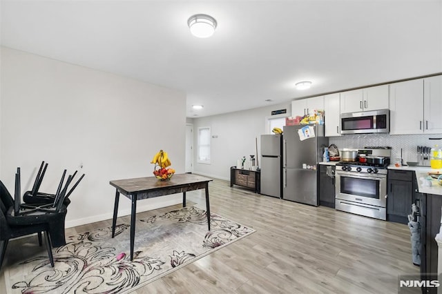 kitchen featuring white cabinets, stainless steel appliances, light hardwood / wood-style flooring, and tasteful backsplash