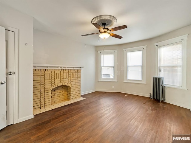 unfurnished living room with ceiling fan, radiator heating unit, a brick fireplace, and dark hardwood / wood-style flooring