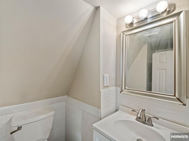 bathroom featuring toilet, vanity, and tile walls