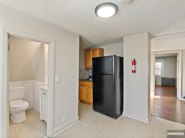 kitchen featuring tile walls, tasteful backsplash, radiator, light tile patterned floors, and black fridge