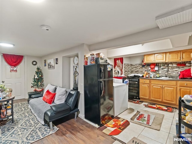 kitchen featuring tasteful backsplash, gas range oven, sink, black fridge, and light tile patterned flooring