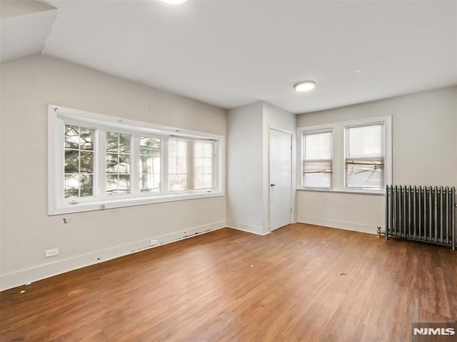 spare room featuring hardwood / wood-style floors, radiator heating unit, and vaulted ceiling