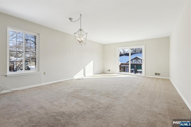 unfurnished room with light colored carpet, a notable chandelier, and a wealth of natural light