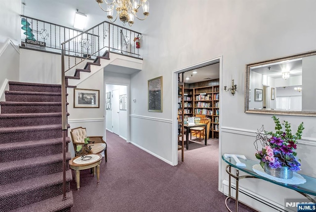 staircase featuring built in shelves, a chandelier, baseboard heating, carpet floors, and a high ceiling