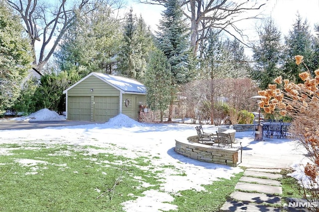 yard layered in snow featuring a patio area, an outbuilding, an outdoor fire pit, and a garage